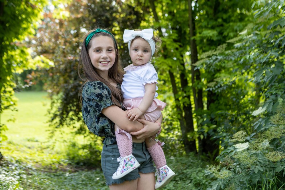 sorelle figlie famiglia giardino parco natura fiocco sorrisi felici smorfie abbraccio servizio fotografico