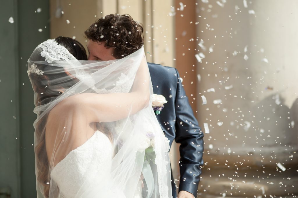 foto sposi appena sposati mentre il riso li avvolge fuori dalla chiesa bacio sulla fronte servizio fotografico matrimonio fotografo cerimonia carpi