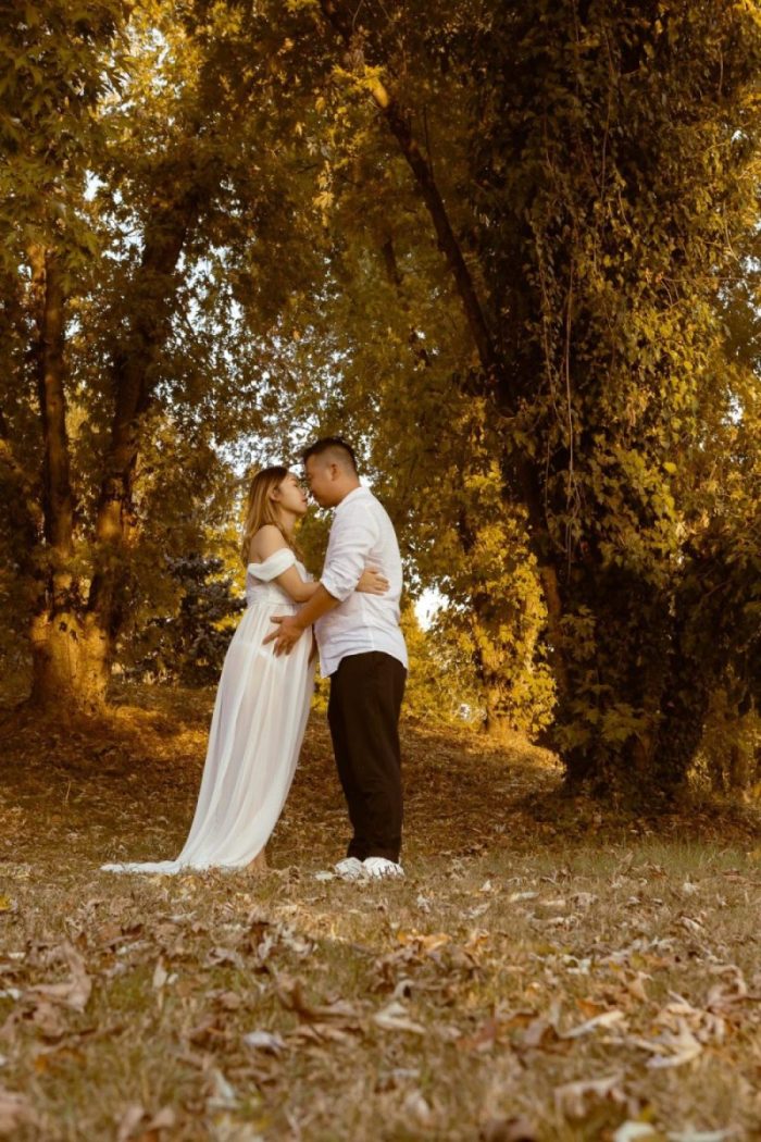 coppia bacio gravidanza maternità donna incinta futura famiglia futuri genitori parco alberi foglie vestiti bianchi dolce attesa