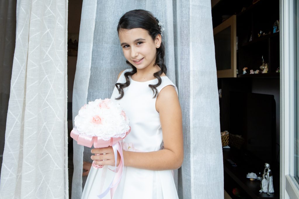 bambina comunione vestito bianco cintura fiori rosa sorriso evento cerimonia acconciatura boccoli bouquet di fiori vestito da cerimonia comunione cresima fotografo