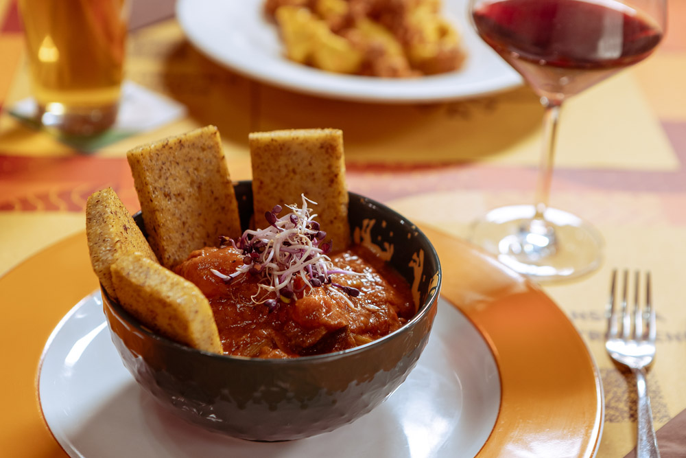 Piatto di stufato con polenta abbinato a un calice di vino rosso