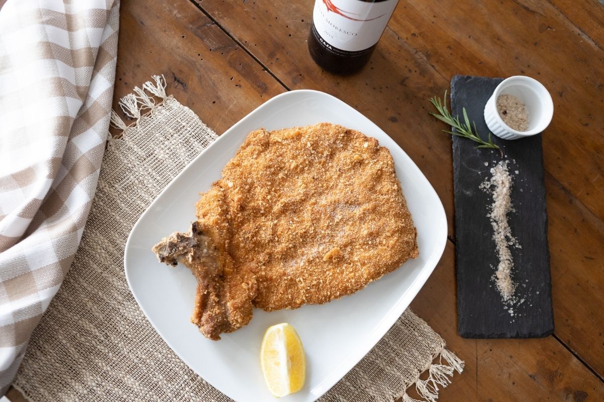 Cotoletta impanata servita con limone in abbinamento a un calice di vino